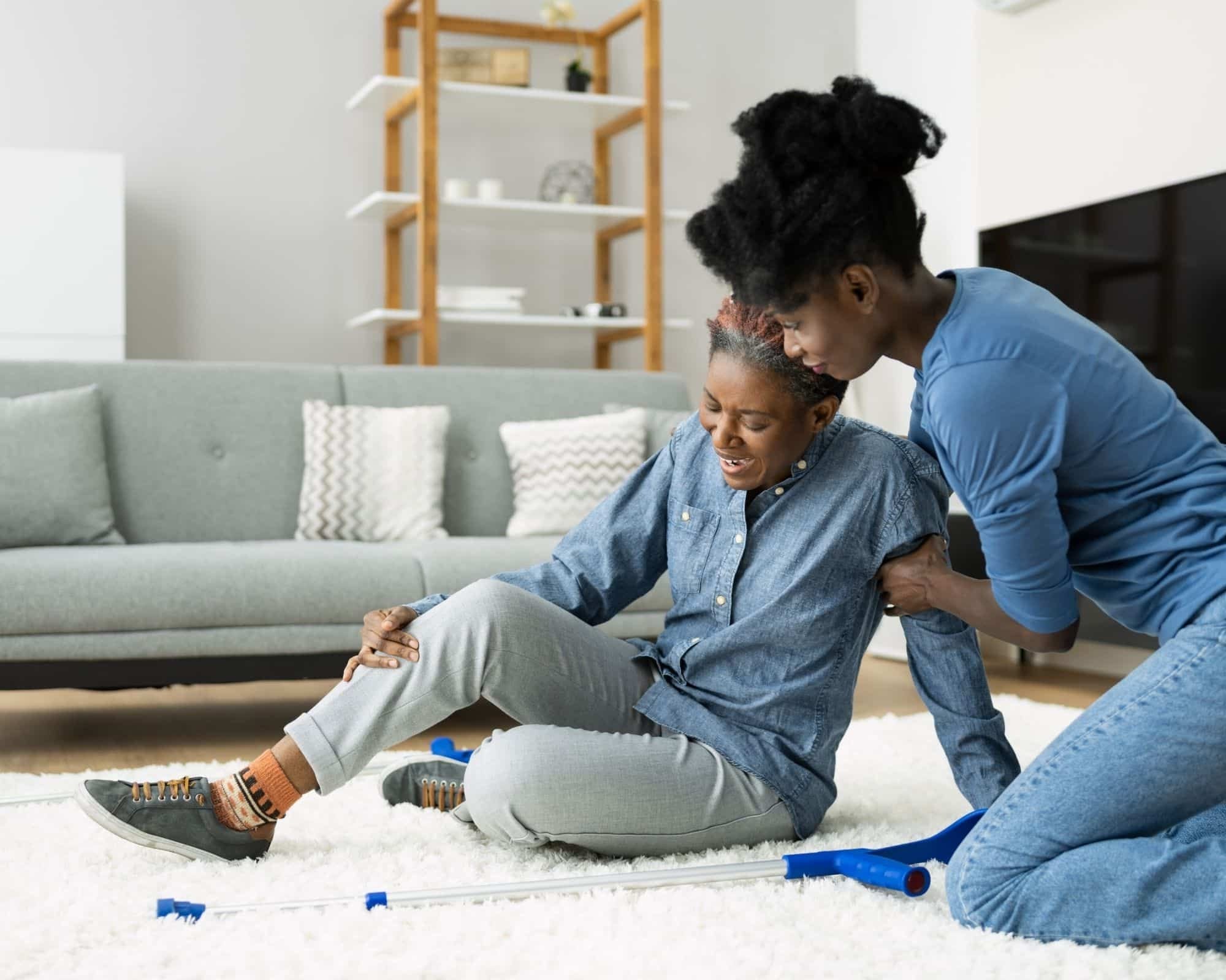 Düşme riski sebebiyle yere düşmüş ve yanındaki kadından yardım alan bir yaşlı kadın