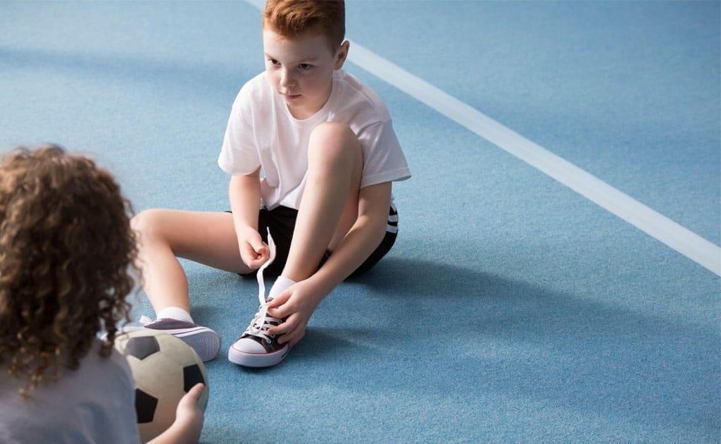 çocuklarda spor yaralanmalarına karşı bağcıklarını bağlayan bir erkek çocuk